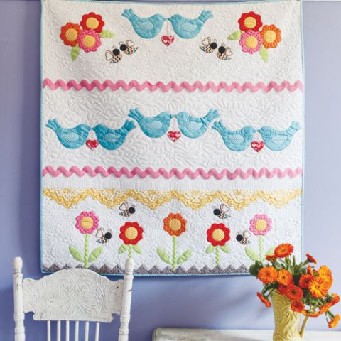 Bird, bee and flower appliqué and english paper pieced wallhanging quilt styled shot hanging up with flowers