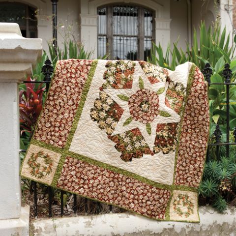 Styled shot of floral themed quilt with hexagon and star in the centre draped over fence