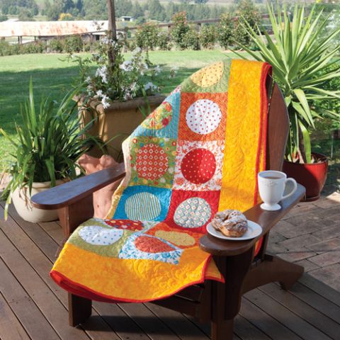 Styled shot of bright yellow circle pattern quilt draped over chair on verandah