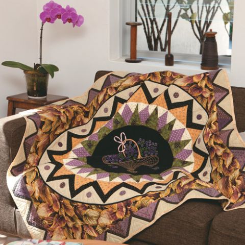 Styled shot of appliqué and foundation pieced medallion quilt with vintage embroidery centre draped over couch