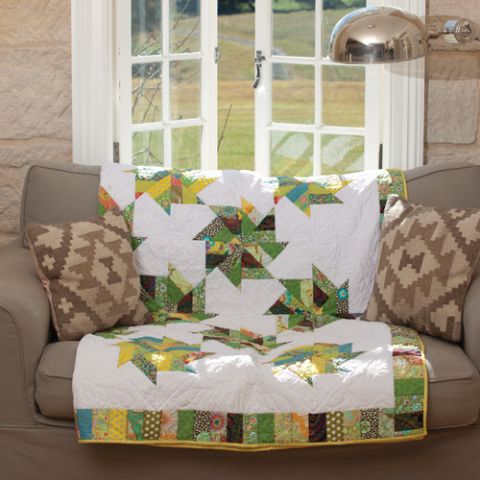 Styled shot of quilt with green patchwork windmill pattern lying on lounge in living room