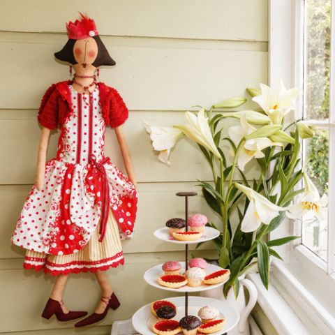 Styled shot of gertrude doll wearing red and white polka dot dress, crown and jewellery next to cupcake stand