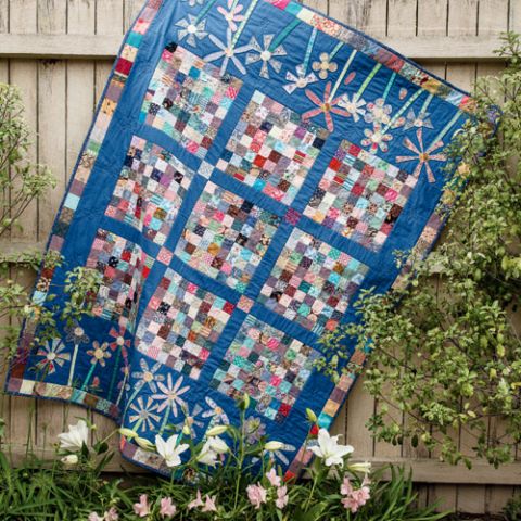 Styled shot of appliqué flower and patchwork scrappy quilt hanging in garden