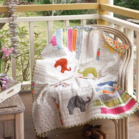 Styled shot of modern elephant appliqué cot quilt draped over chair