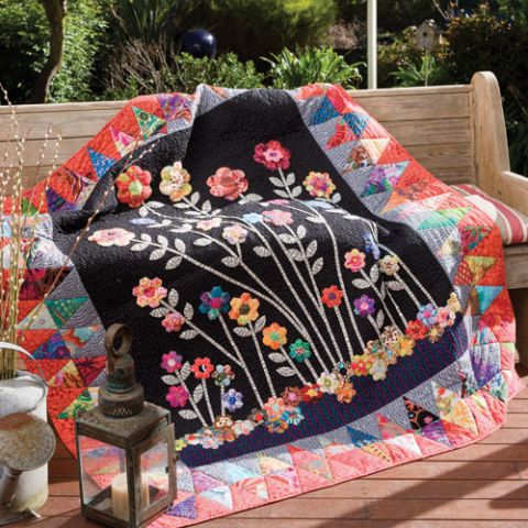 Styled shot of appliqué and english paper pieced flower garden quilt outdoors draped over bench