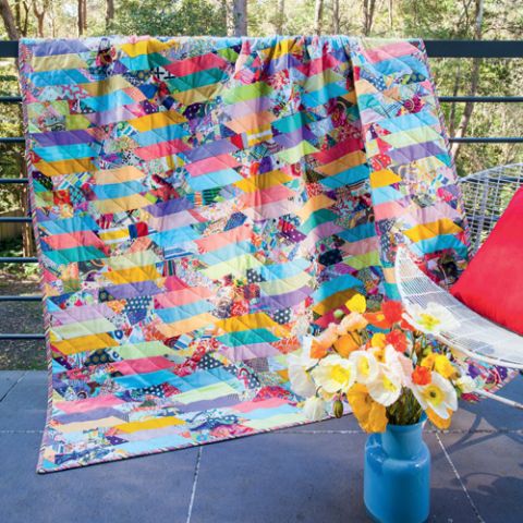 Styled shot of modern scrappy geometric quilt draped over railing