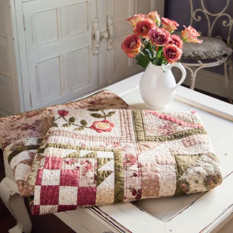 Styled shot of traditional style patchwork and appliqué quilt folded on table with vase of flowers