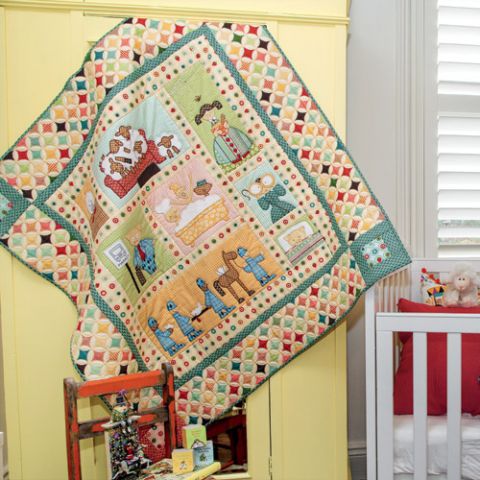 Styled shot of nursery rhyme appliqué quilt hanging up near cot