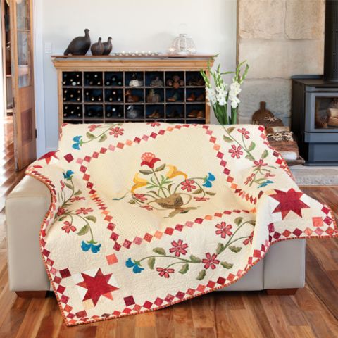 Styled shot of quilt with flower borders and feature flower vase in the centre draped over lounge