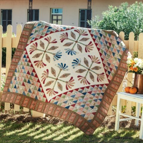Styled shot of appliqué flower and patchwork triangles quilt draped over fence