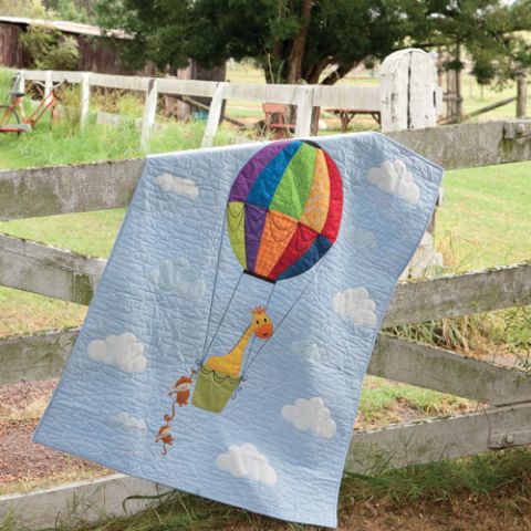 Styled shot of appliqué hot air balloon baby's cot quilt draped over fence