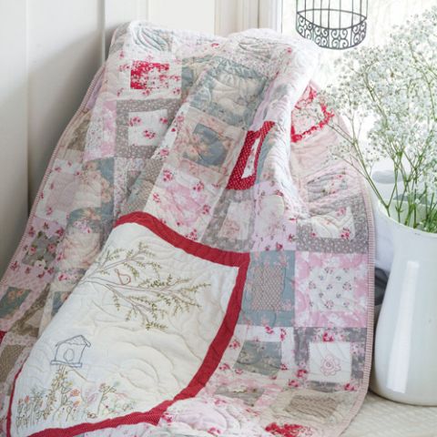 Styled shot of pretty embroidered patchwork quilt draped with flowers